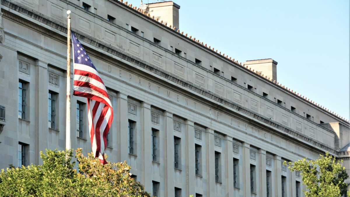 The facade of the Department of Justice building in Washington, D.C., behind a U.S. flag.